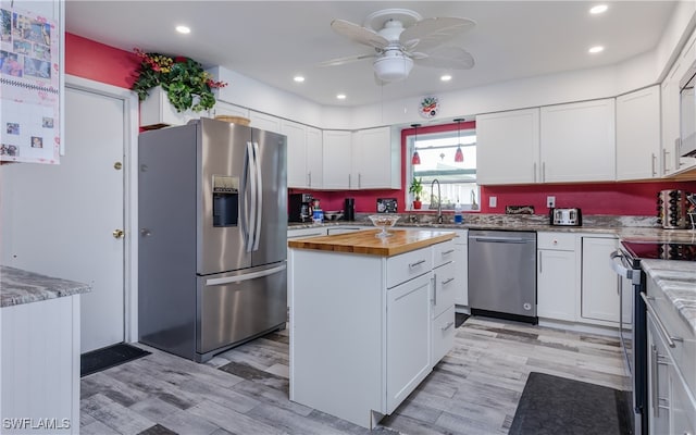 kitchen with stainless steel appliances, butcher block countertops, white cabinetry, and light wood-type flooring