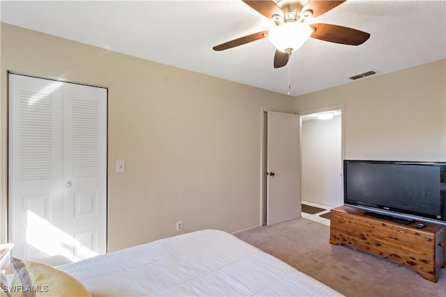 bedroom with ceiling fan, a textured ceiling, a closet, and light colored carpet