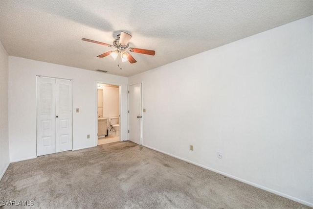 unfurnished bedroom with a textured ceiling, ensuite bathroom, carpet flooring, visible vents, and a closet