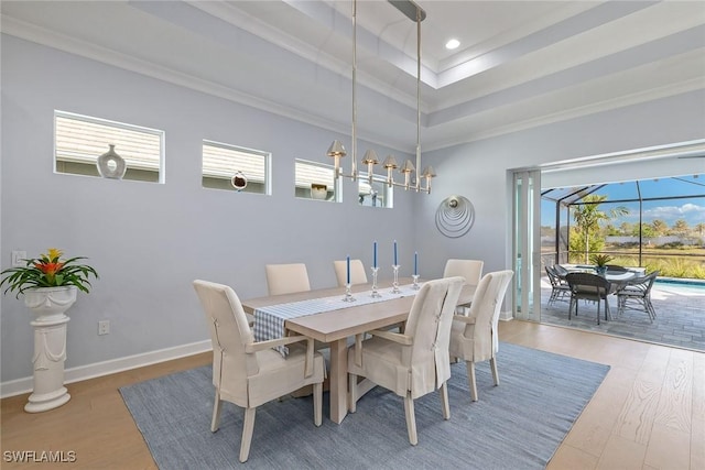 dining room with a raised ceiling, a healthy amount of sunlight, crown molding, and wood-type flooring