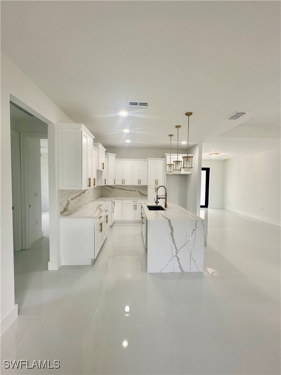 kitchen featuring light stone counters, a kitchen island, white cabinetry, pendant lighting, and sink