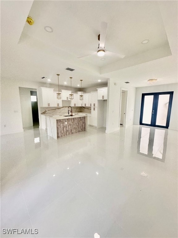 unfurnished living room with light tile patterned flooring, ceiling fan, sink, and a tray ceiling