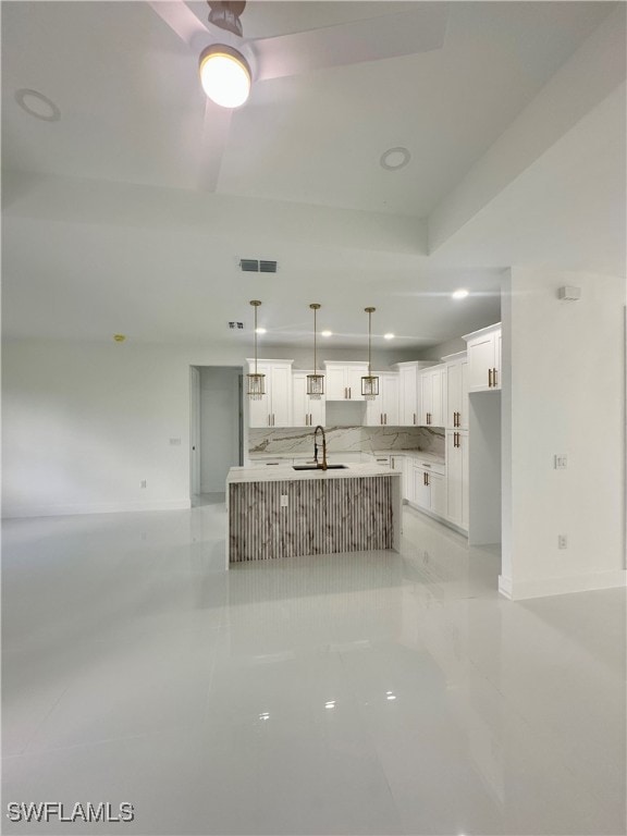 kitchen with decorative light fixtures, white cabinetry, sink, and an island with sink