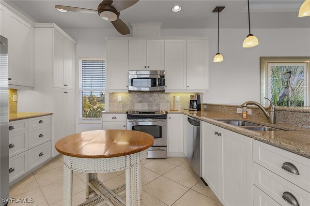 kitchen featuring light stone counters, stainless steel appliances, white cabinetry, hanging light fixtures, and sink