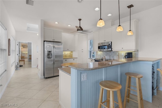 kitchen with kitchen peninsula, a breakfast bar area, backsplash, white cabinetry, and appliances with stainless steel finishes