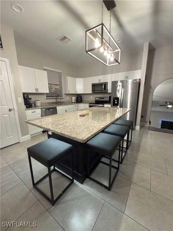 kitchen with hanging light fixtures, stainless steel appliances, a kitchen island, a breakfast bar area, and white cabinets