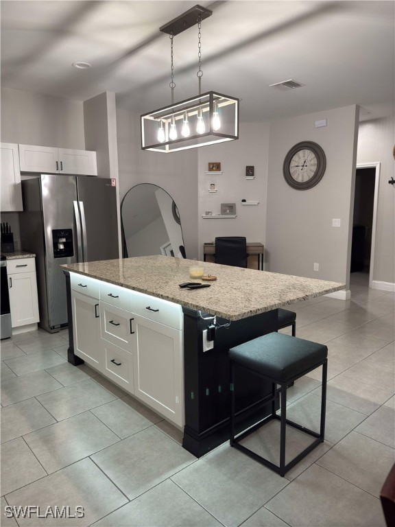 kitchen with stainless steel refrigerator with ice dispenser, light stone counters, a kitchen island, decorative light fixtures, and white cabinetry