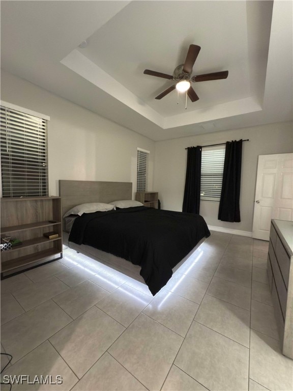 bedroom featuring ceiling fan, a raised ceiling, and light tile patterned floors