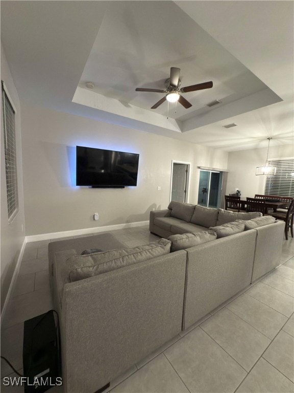 tiled living room with ceiling fan and a raised ceiling