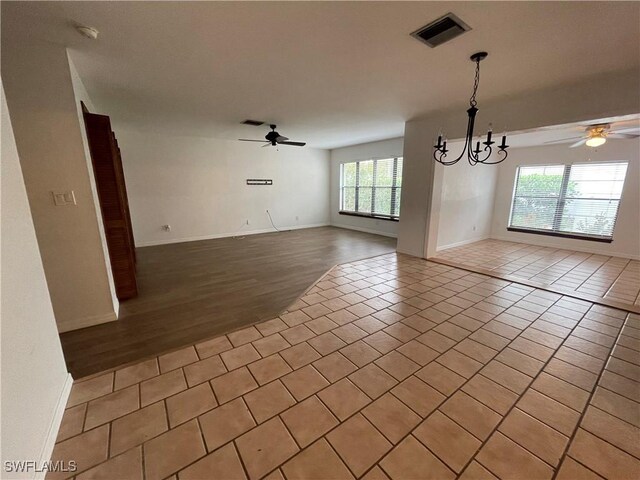 empty room with ceiling fan with notable chandelier and light tile patterned floors