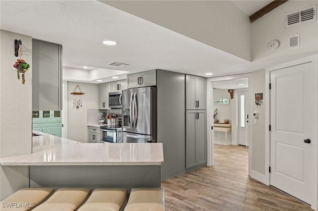 kitchen featuring gray cabinets, kitchen peninsula, a breakfast bar, and stainless steel appliances