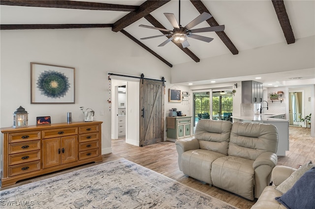 living room featuring light hardwood / wood-style floors, sink, beam ceiling, high vaulted ceiling, and a barn door