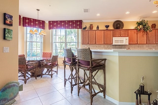 kitchen with backsplash, crown molding, a kitchen bar, and decorative light fixtures