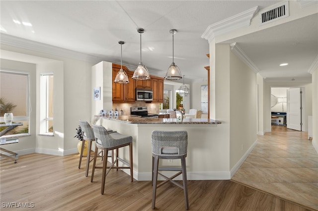 kitchen featuring kitchen peninsula, appliances with stainless steel finishes, a kitchen breakfast bar, light hardwood / wood-style flooring, and stone counters