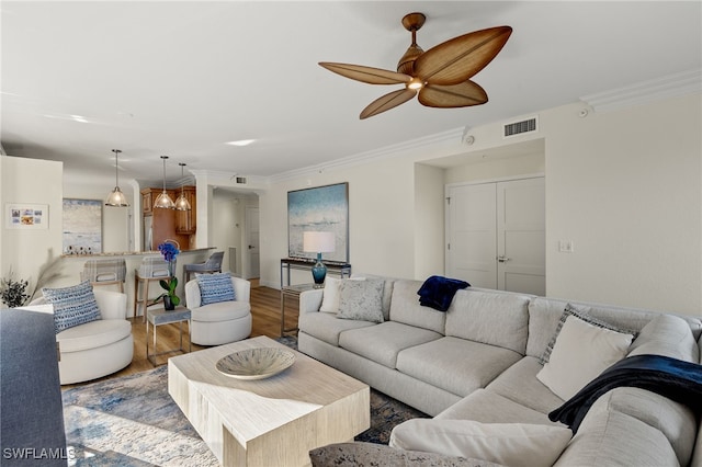 living room with ceiling fan, ornamental molding, and light wood-type flooring