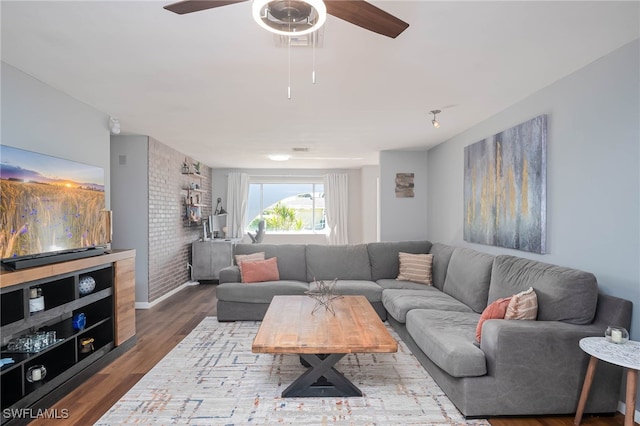 living room featuring ceiling fan, wood-type flooring, and brick wall