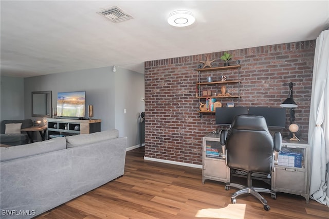 home office with hardwood / wood-style flooring and brick wall