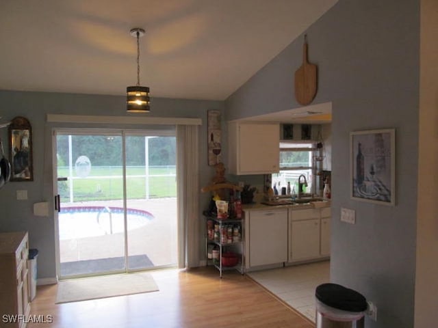 kitchen with white cabinetry, decorative light fixtures, sink, vaulted ceiling, and light hardwood / wood-style floors