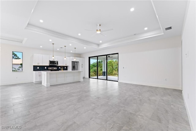 unfurnished living room featuring ceiling fan and a tray ceiling