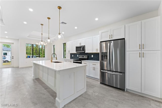 kitchen featuring decorative light fixtures, sink, white cabinets, stainless steel appliances, and a center island with sink