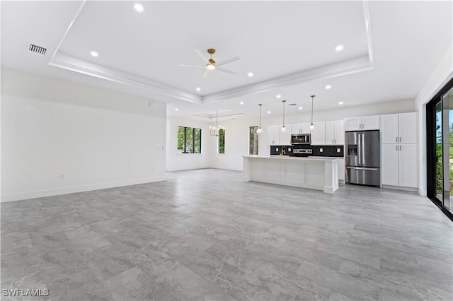 unfurnished living room featuring recessed lighting, ceiling fan with notable chandelier, visible vents, baseboards, and a tray ceiling