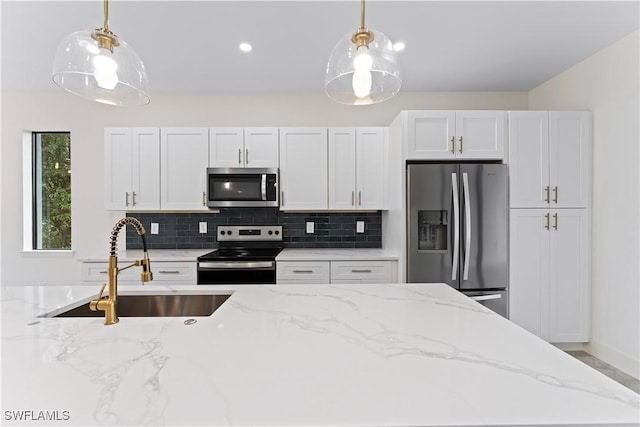 kitchen with stainless steel appliances, white cabinetry, hanging light fixtures, and light stone counters