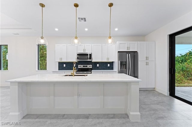 kitchen with light stone countertops, white cabinets, appliances with stainless steel finishes, and a center island with sink