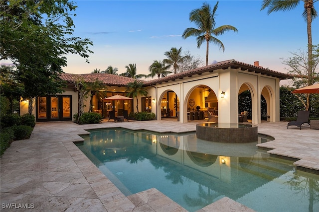 pool at dusk featuring french doors and a patio area