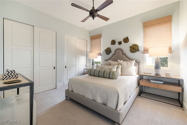 bedroom with ceiling fan, light carpet, and two closets