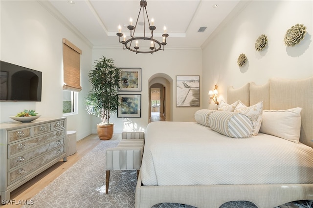 bedroom featuring a tray ceiling, an inviting chandelier, ornamental molding, and light hardwood / wood-style flooring