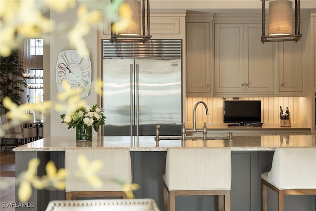 kitchen featuring built in fridge, light stone counters, hardwood / wood-style flooring, a breakfast bar area, and tasteful backsplash