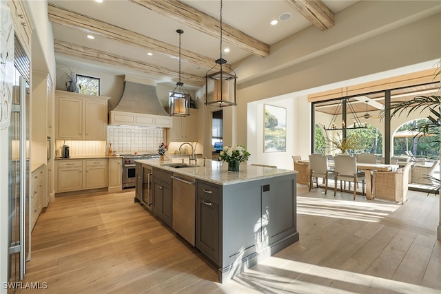 kitchen with stainless steel appliances, light hardwood / wood-style floors, a kitchen island with sink, custom range hood, and beamed ceiling