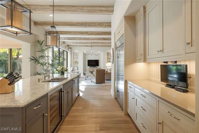 kitchen with light stone counters, wine cooler, beam ceiling, hanging light fixtures, and light hardwood / wood-style flooring