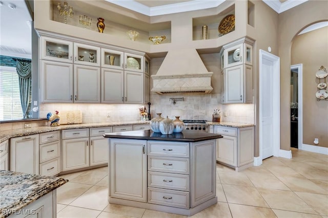 kitchen with light tile patterned floors, tasteful backsplash, a kitchen island, custom exhaust hood, and ornamental molding