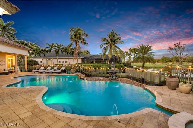 pool at dusk featuring pool water feature, a patio area, and outdoor lounge area