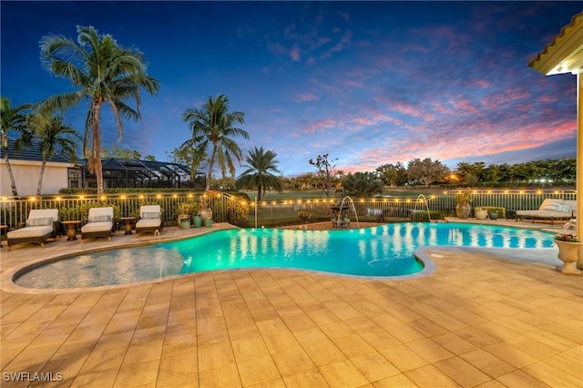 pool at dusk featuring pool water feature and a patio