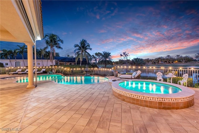 pool at dusk featuring pool water feature, a patio, and a hot tub