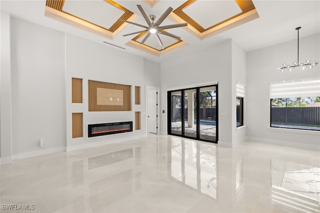 unfurnished living room featuring ceiling fan with notable chandelier, a wealth of natural light, a high ceiling, and coffered ceiling