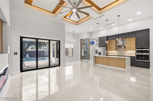 kitchen featuring stainless steel appliances, coffered ceiling, a large island, wall chimney range hood, and pendant lighting