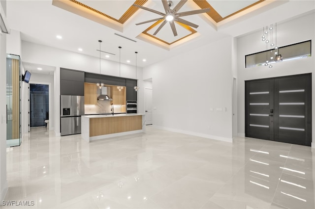 kitchen with stainless steel appliances, a high ceiling, decorative light fixtures, a center island, and wall chimney range hood