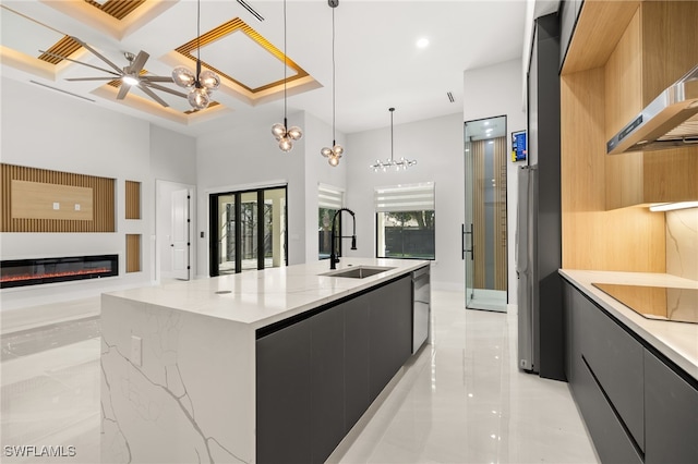 kitchen with decorative light fixtures, black electric cooktop, sink, a kitchen island with sink, and a high ceiling