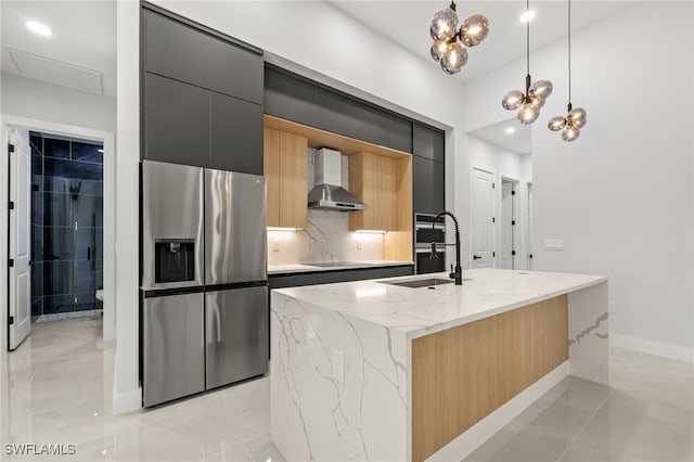 kitchen featuring a center island with sink, hanging light fixtures, sink, stainless steel fridge with ice dispenser, and wall chimney range hood