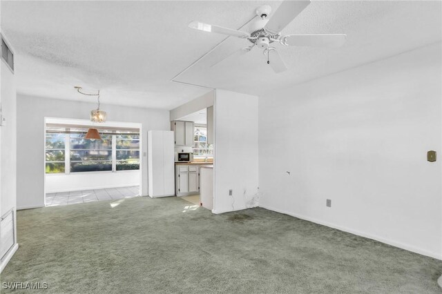 unfurnished living room with a ceiling fan, visible vents, light carpet, and a textured ceiling