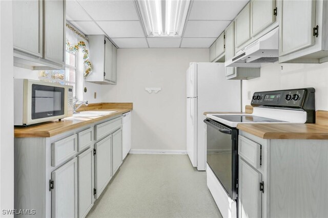 kitchen featuring a sink, white appliances, a drop ceiling, under cabinet range hood, and baseboards