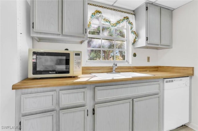 kitchen with butcher block countertops, white appliances, and a sink