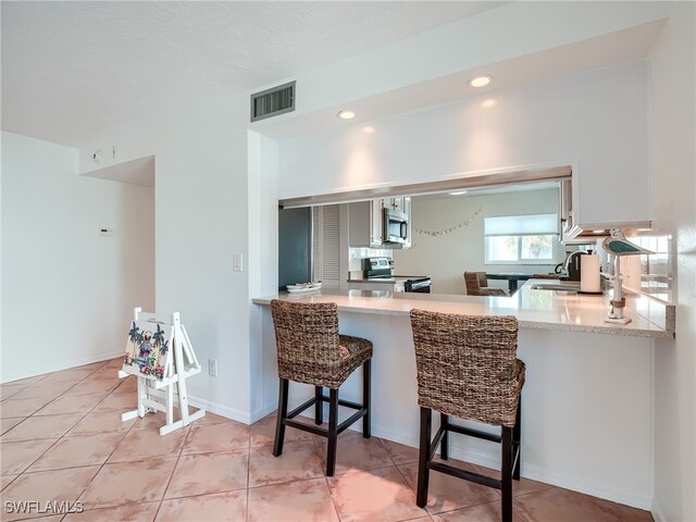 kitchen with a kitchen breakfast bar, sink, light tile patterned floors, kitchen peninsula, and stainless steel appliances