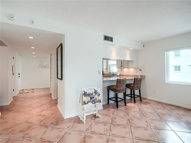 kitchen featuring white cabinetry, sink, kitchen peninsula, a breakfast bar area, and light tile patterned floors