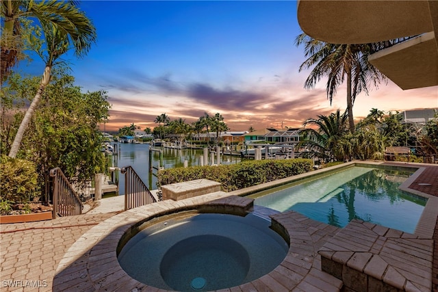 pool at dusk with an in ground hot tub and a water view