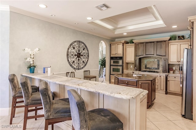 kitchen featuring stainless steel appliances, an island with sink, a kitchen breakfast bar, a raised ceiling, and light stone countertops