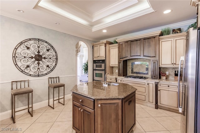 kitchen with crown molding, a center island with sink, sink, and a tray ceiling